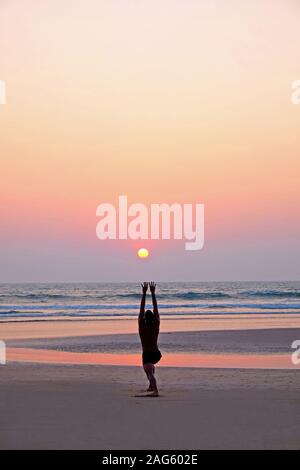 Eine nicht erkennbare Mann eine Yoga Pose, das Sonnengebet, auf einer weiten leeren Sandstrand, seine Beine verbogen sind mit ausgestreckten Armen, er ist Lin Stockfoto