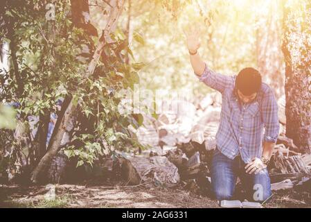 Männlich auf den Knien auf dem Boden mit der Hand In Richtung Himmel mit der Sonne, die im Hintergrund scheint Stockfoto