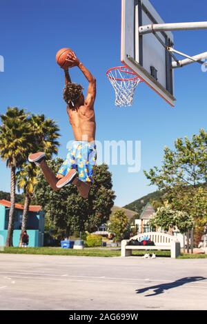 Männchen mit blauen und gelben Shorts machen einen Dunk in Der Basketballplatz tagsüber Stockfoto