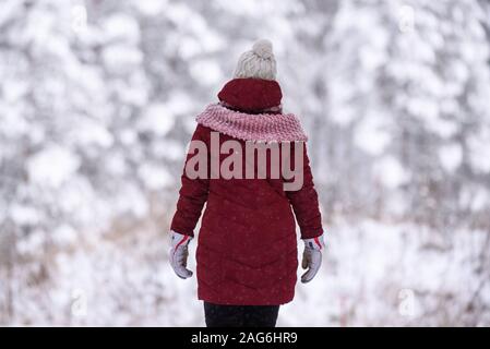 GULBENE, Lettland. 24. Dezember 2018. Frau das Tragen der roten Winterjacke, Wanderungen im verschneiten Wald. Verschneite Bäume und Wald Trail. Stockfoto