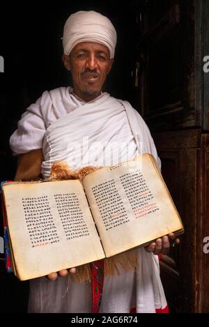 Äthiopien, Amhara, Lalibela, Mount Abuna Yosef, Inside, asheton Maryam Kloster, Priester an der Tür halten alte Evangelium in Ge'ez Script auf Pergament Stockfoto