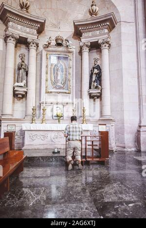 Vertikale Aufnahme eines Mannes auf den Knien beim Beten Die Kirche Stockfoto