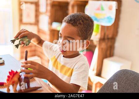 Schöne afrikanische amerikanische Kleinkind spielen mit Dinosaurier Spielzeug auf dem Schreibtisch im Kindergarten Stockfoto