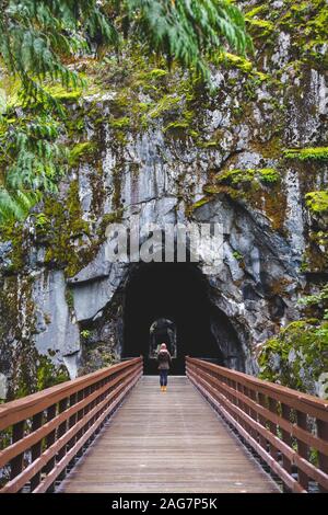 Vertikale Aufnahme einer Frau, die in einem natürlichen Tunnel läuft Durch eine Brücke Stockfoto