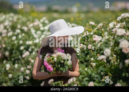 Schöne Frau im Retro-stil Polka Dot kleid und hut Holding ein zarter Strauss aus der Bulgarischen rosa und weiß frische Rosen im Frühjahr warmen sonnigen Tag wit Stockfoto