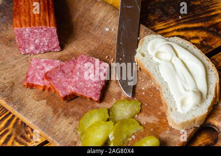 Schnelles Frühstück vor dem Arbeitstag. Zutaten für ein Sandwich. Scheiben Salami, Gurken und Knäckebrot mit weißer Soße. Fett Kalorien essen. Stockfoto
