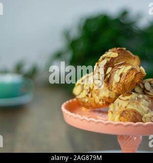 Almond Croissants auf Kuchen stand mit viel Grün und Kaffee Stockfoto