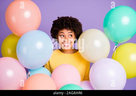 Foto von charmanten Fröhlich niedlich schön genießen schwarz Youngster tragen gelbe Pullover lächelnd toothily umgeben mit Luftballons multicolor isoliert Stockfoto