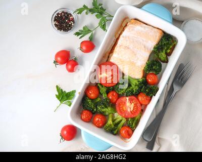 Fisch Lachs im Ofen gebacken mit Gemüse - Brokkoli, Tomaten. Gesunde Ernährung Essen, der weiße Marmor Hintergrund, Ansicht von oben. Stockfoto