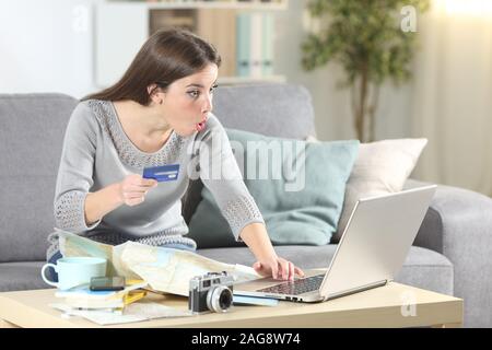 Überrascht touristische Zahlen Sie Online mit Kreditkarte Planung Urlaub auf einer Couch im Wohnzimmer zu Hause sitzen Stockfoto