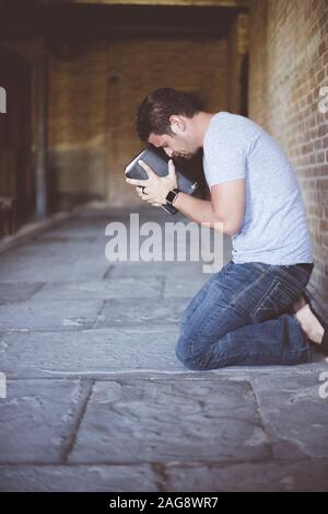 Vertikale Aufnahme eines Mannes auf den Knien auf der Boden mit der bibel gegen seinen Kopf beten Stockfoto