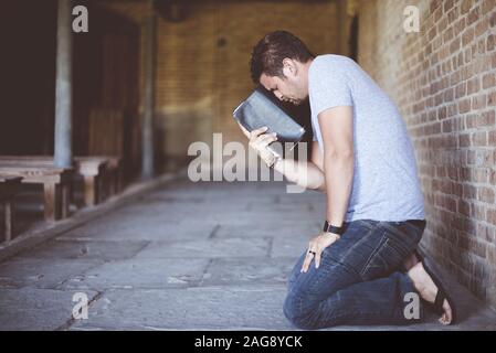 Nahaufnahme eines Männchens auf den Knien mit Die bibel gegen seinen Kopf beim Beten Stockfoto