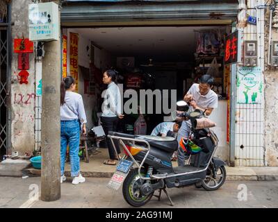 HAIKOU, HAINAN, CHINA - Mar 2 2019 - ein Mechaniker Reparaturen einen Elektroroller an einem traditionellen kleine Motorrad Werkstatt / Workshop in Haikou. Stockfoto