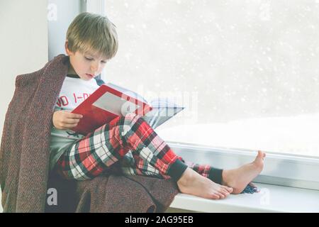 Kind liest Buch durch das Fenster. Schönes Winterwetter mit Schnee Stockfoto