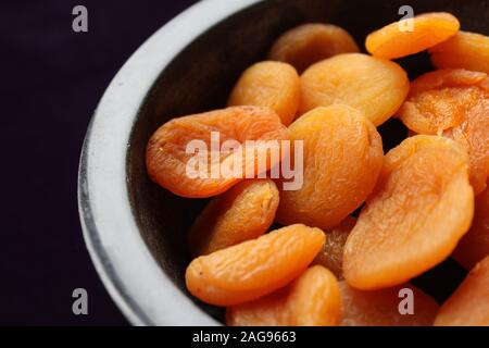 Nahaufnahme von getrockneten Aprikosen in einem schwarzen Marmor Schüssel, gegen einen dunklen Tisch in Lila Hintergrund Tuch. Stockfoto