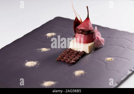 Köstliches Dessert mit roter Birne und Schokolade auf einem schwarzen Oberfläche Stockfoto