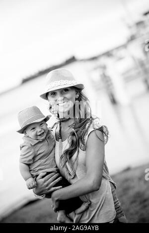 Vertikale Graustufenaufnahme einer Mutter, die ihr Kind hält Lächelnd auf die Kamera Stockfoto