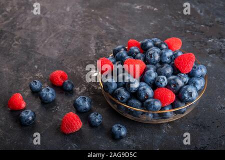 Frische Blaubeeren und Erdbeeren in eine Glasschüssel und auf einem dunklen Hintergrund, Ansicht von oben Stockfoto
