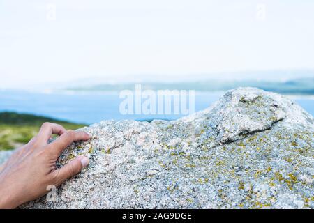 Nahaufnahme der Hand eines jungen kaukasischen Mann, greifen die Felsen von einer Felsformation an der Südküste von Korsika, Frankreich, mit dem Mittelmeer se Stockfoto