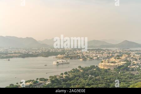 Erhöhten Blick auf Lake Pichola durch City Palace flankiert, Lake Palace, und Aravalli Hills bei Sonnenaufgang im Sommer in Udaipur, Rajasthan, Indien. Stockfoto