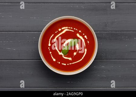 Eine Schüssel leckere Tomatensuppe, garniert mit ein wenig Sahne und einem Zweig Basilikum, in einer rustikalen Schüssel, Schuß auf einen aufgeregten dunklen Hintergrund. Stockfoto
