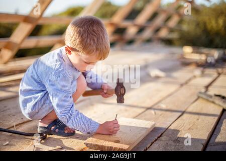Kind (junge) Hammer Nägel mit einem Hammer in einer Holzplatte auf dem Dach Stockfoto