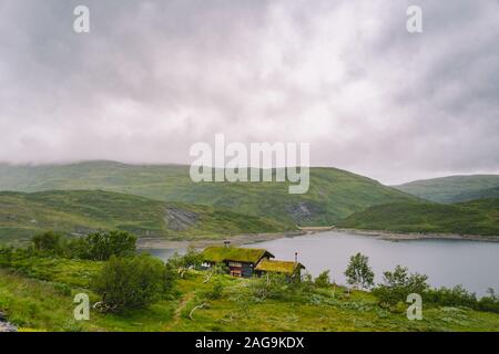 Norwegische Holz- Sommer Haus mit Blick auf den malerischen See, Norwegen, Skandinavien. Ferienhaus am See in Ländlichen. Torf überdachte Hütte am See. Typische Gras überdacht Stockfoto