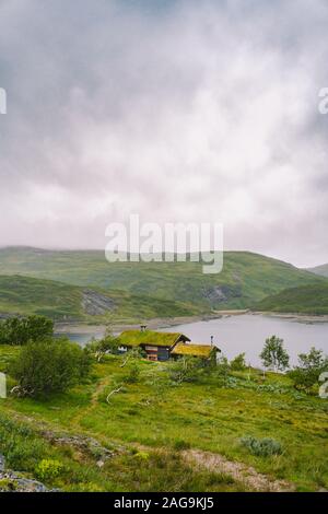 Norwegische Holz- Sommer Haus mit Blick auf den malerischen See, Norwegen, Skandinavien. Ferienhaus am See in Ländlichen. Torf überdachte Hütte am See. Typische Gras überdacht Stockfoto