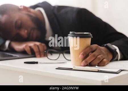 Erschöpft Bürokaufmann/-holding Tasse Kaffee, schlafen am Arbeitsplatz Stockfoto