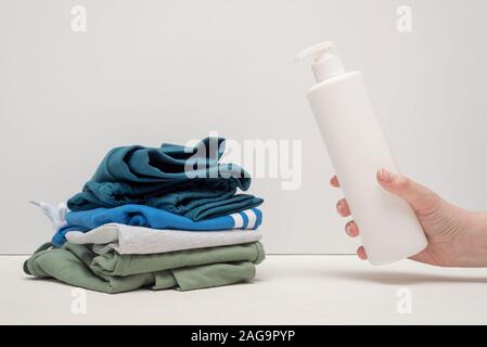 Reinigungsmittel Flasche in weiblicher Hand Nahaufnahme und schmutzige Kleidung auf weißem Hintergrund. Stockfoto