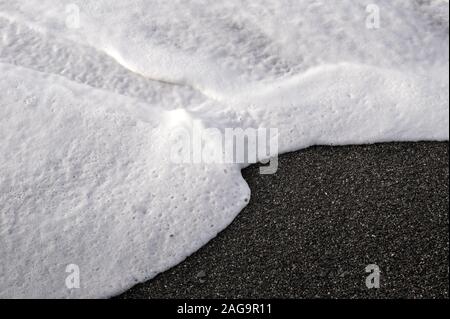 White sea Foam am Strand Kies durch die raue See und starkem Wind verursacht Stockfoto