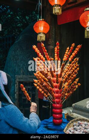 Frau kauft und hält traditionelle chinesische Dessert Tanghulu auch bingtanghulu genannt, ist ein Snack von kandierten Früchten. Weißdorn-Gourd karamellisiert sauer. Stockfoto