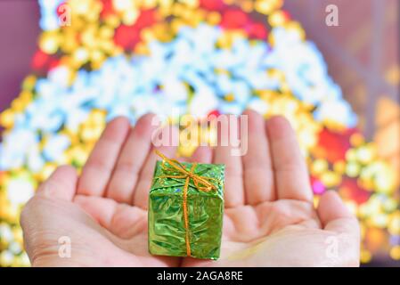 Hand, die kleine Weihnachtsgeschenk mit Weihnachtsbaum als Hintergrund Stockfoto