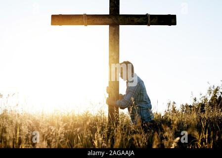 Männchen mit dem Kopf lehnte sich an eine Hand aus Holz Kreuz beim Beten Stockfoto