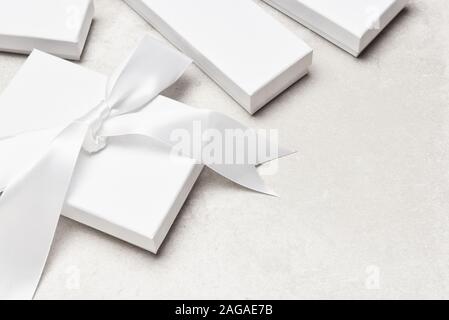 High Angle Shot einer Gruppe von weißen Geschenk Boxen auf einem hellgrauen Desk Top. Eine Box hat eine große weiße Schleife. Stockfoto