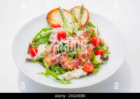 Gemischter Salat mit gebratenen Speck geriebenen Käse, Weichkäse und Tomaten. als Dekoration Spargel und Brot Stockfoto