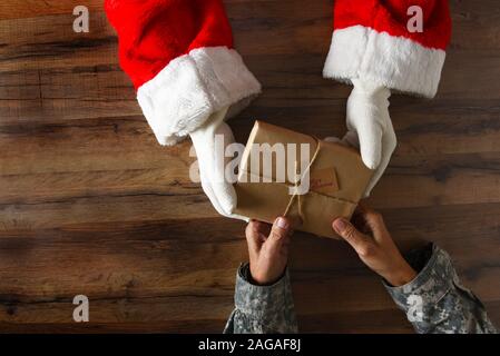 Santa Claus Übergabe einer einfachen eingewickelt zu Weihnachten ein Soldat. High Angle Shot nur mit Händen und Armen sichtbar. Stockfoto