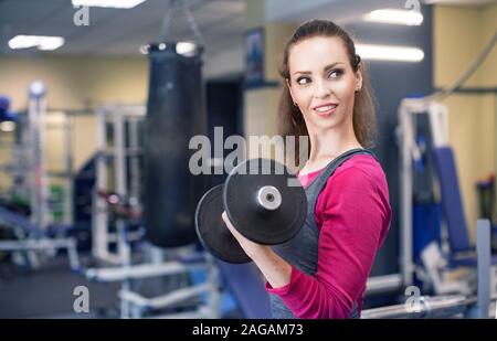 Lächelnde Frau zieht eine Hantel in der Turnhalle und suchen. Fitness gesunder Lebensstil Konzept. Stockfoto