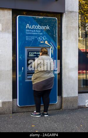 16. Oktober 2019 Eine übergewichtige junge Frau, die ein ATM in der geschäftigen Donegall Square West Belfast Nordirland. Stockfoto