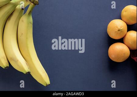 Dunkelblaue Oberfläche mit Bananen und Orangen an den Seiten Stockfoto