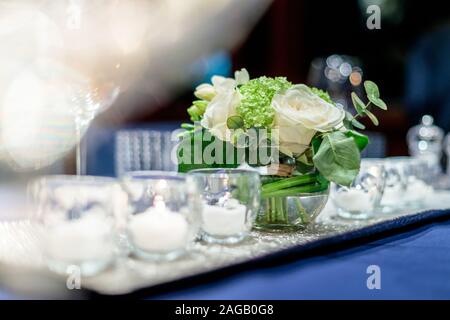 Schöne Blumenkomposition in einer Glasvase mit Glaskerze Halter auf einem blauen Geschirr Stockfoto