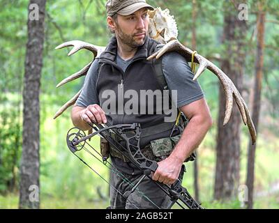 Ein Jäger mit einem Bogen in den Wald führt Moose Hörner auf seinem Rücken und suchen. Close up Portrait. Stockfoto