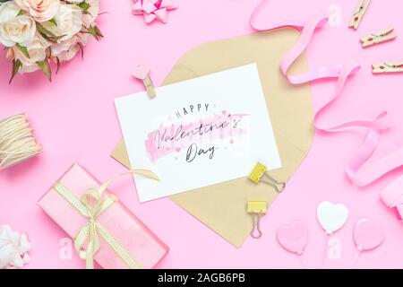 Mockup Postkarte und Umschlag auf rosa Hintergrund mit Happy Valentines Day, Rosen, Blumenstrauß, Geschenkbox, praktische Fertigkeit und Stift. Mock up für elegantes Design. Fl Stockfoto