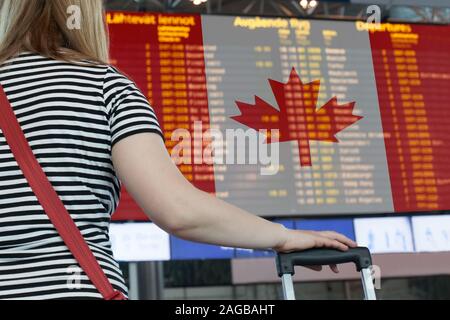 Frau sieht die Anzeigetafel am Flughafen. Wählen Sie ein Land aus Kanada für Reisen oder Migration. Stockfoto