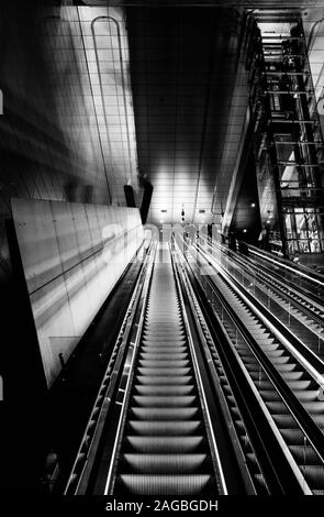 Vertikale Graustufenaufnahme von Menschen auf beleuchteten Rolltreppen Stockfoto