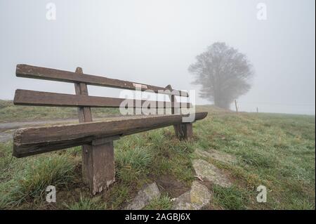 Schöne Aussicht auf eine Holzbank auf einem nebligen Hügel Mit Gras bedeckt Stockfoto