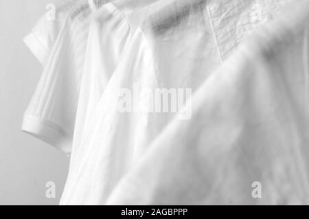 Reihe weißer Baumwolle Kleider hängen auf schwarz Kleiderbügel in einem Rack in einem Shop. Frau minimalistischen Kleiderschrank. Close-up. Stockfoto