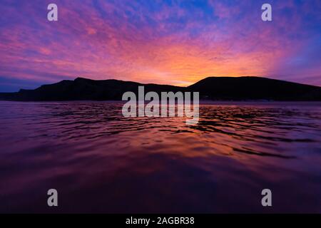 Schöner Sonnenuntergang, der sich auf dem Meer mit Bergsilhouetten spiegelt Der Hintergrund in Portugal Stockfoto