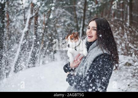 Sehen Sie Schneefall. Smiling brunette Spaß beim Spaziergang mit ihrem Hund im Winter Park Stockfoto