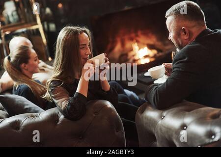 Getränke heißen Tee. Gespräch zwischen jungen und älteren Generation. Freunde der Familie haben schönen Abend am Kamin in luxuriösen, modernen Restaurant Stockfoto